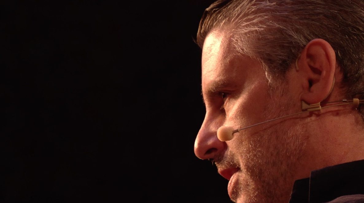 Guillermo Jaramillo de perfil, en escenario con micrófono de diadema