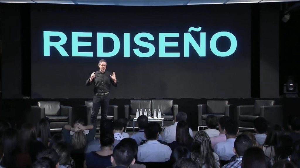 Guillermo en escenario frente a la palabra REDISEÑO en pantalla